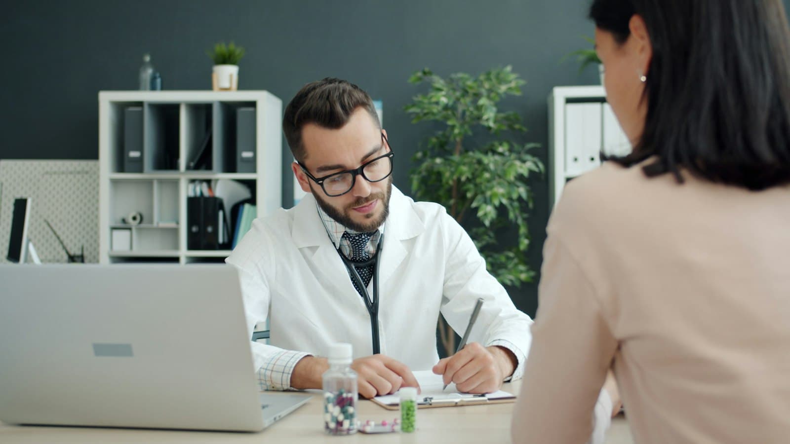 A doctor at his desk taking notes while a patient talks with him