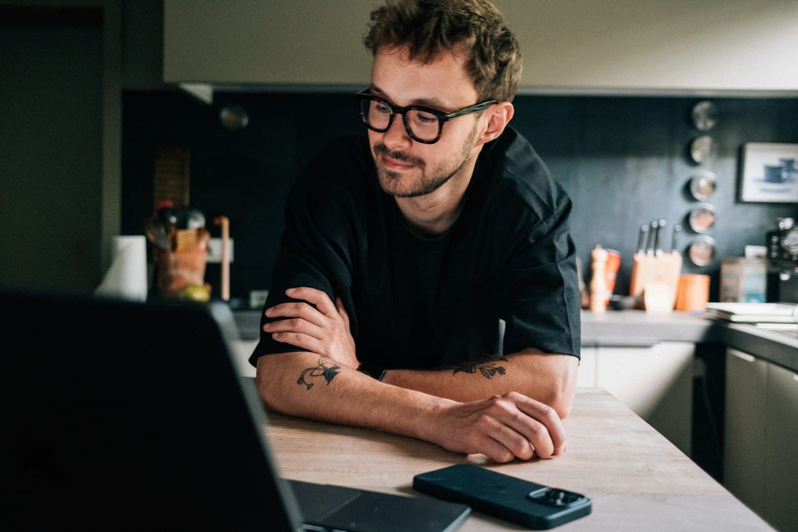 A man leaning on his kitchen counter, looking at an open laptop