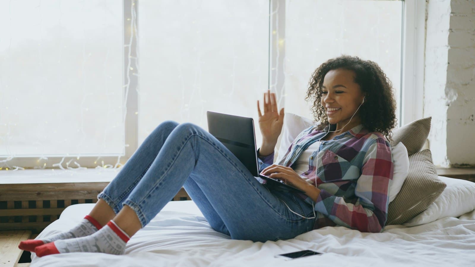 A young woman on her bed waving to someone on a video call