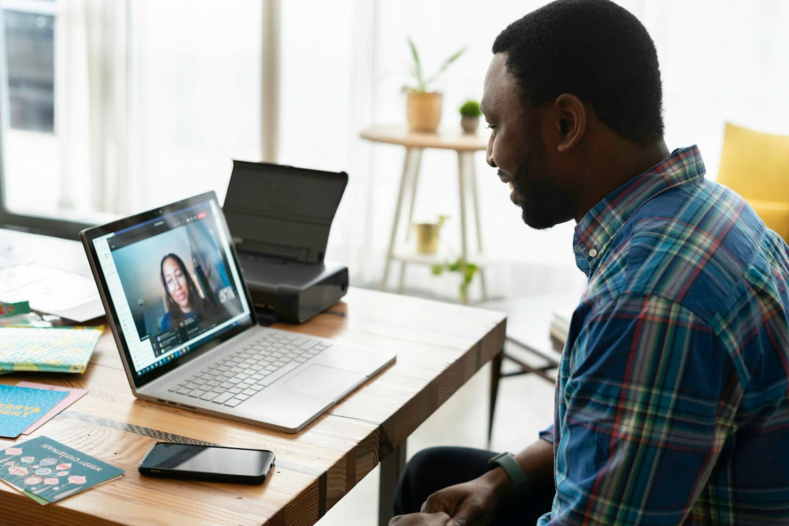 A man in a plaid shirt on a video call with a woman on his laptop at a home desk