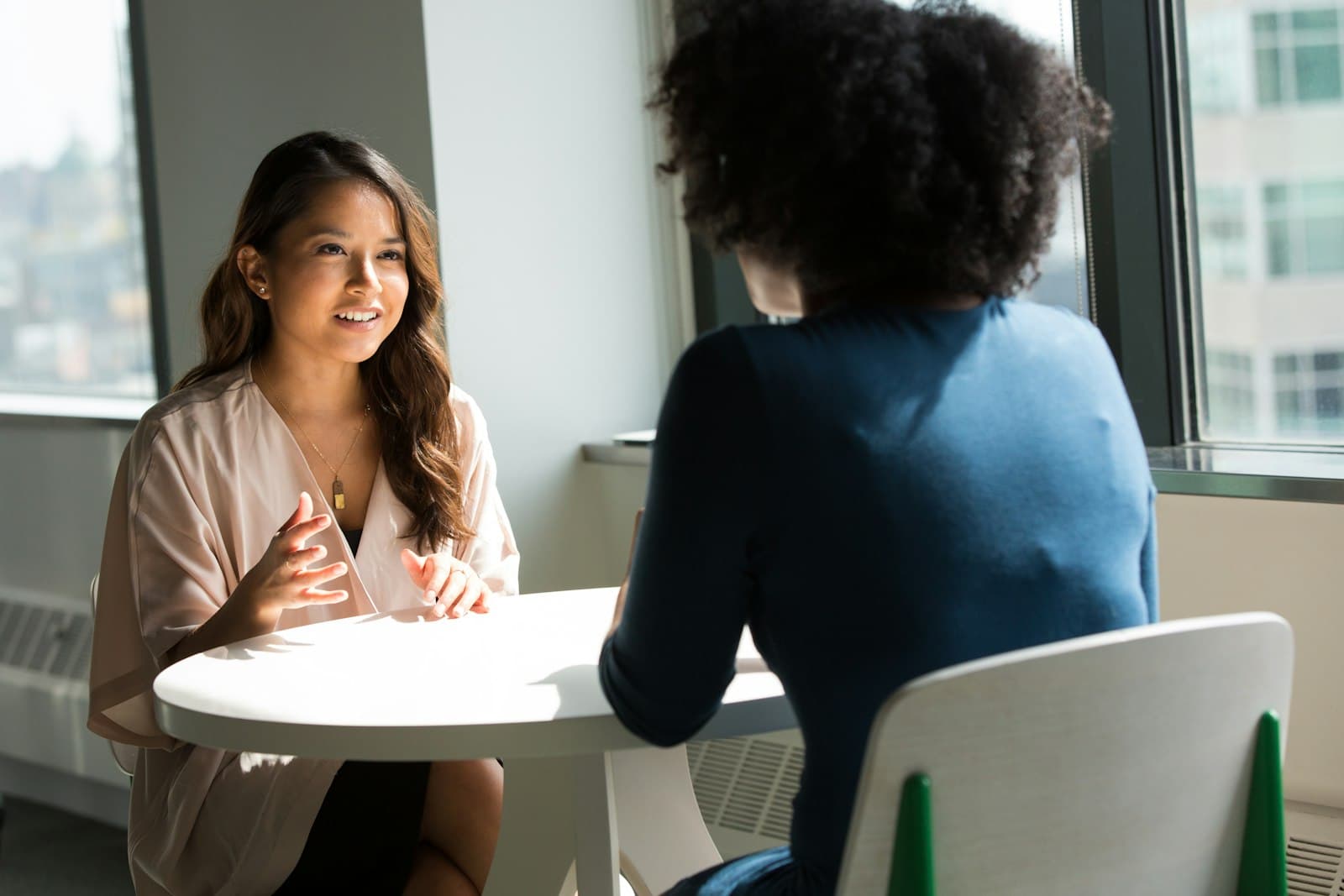 Two women talking across a small round table by a window