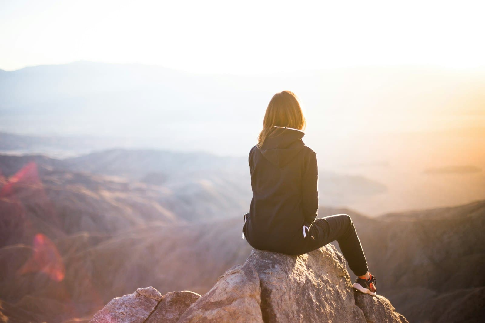 A woman sitting on a rocky peak, looking out over the mountains at sunrise