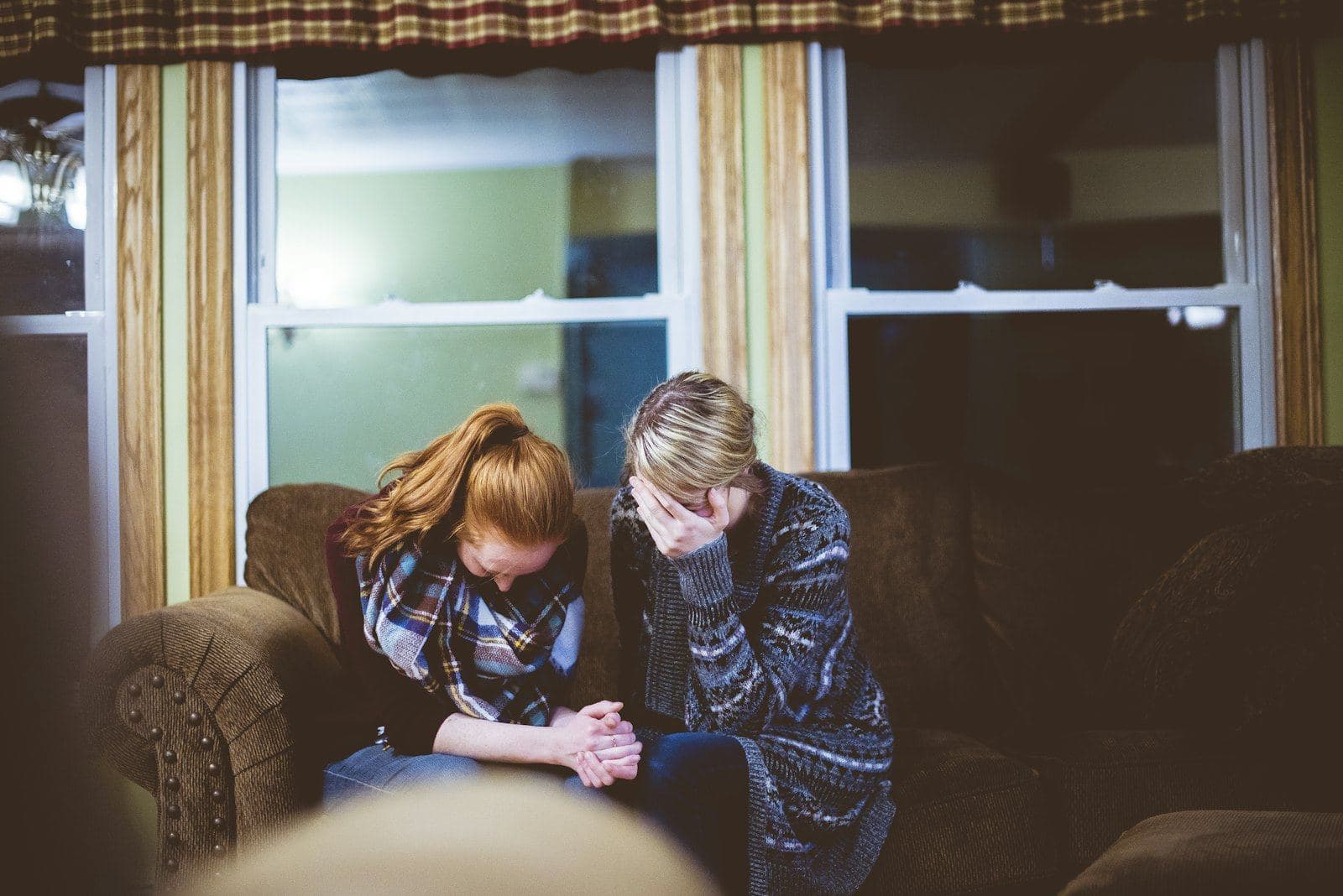 Two women sitting close together on a sofa, one comforting the other