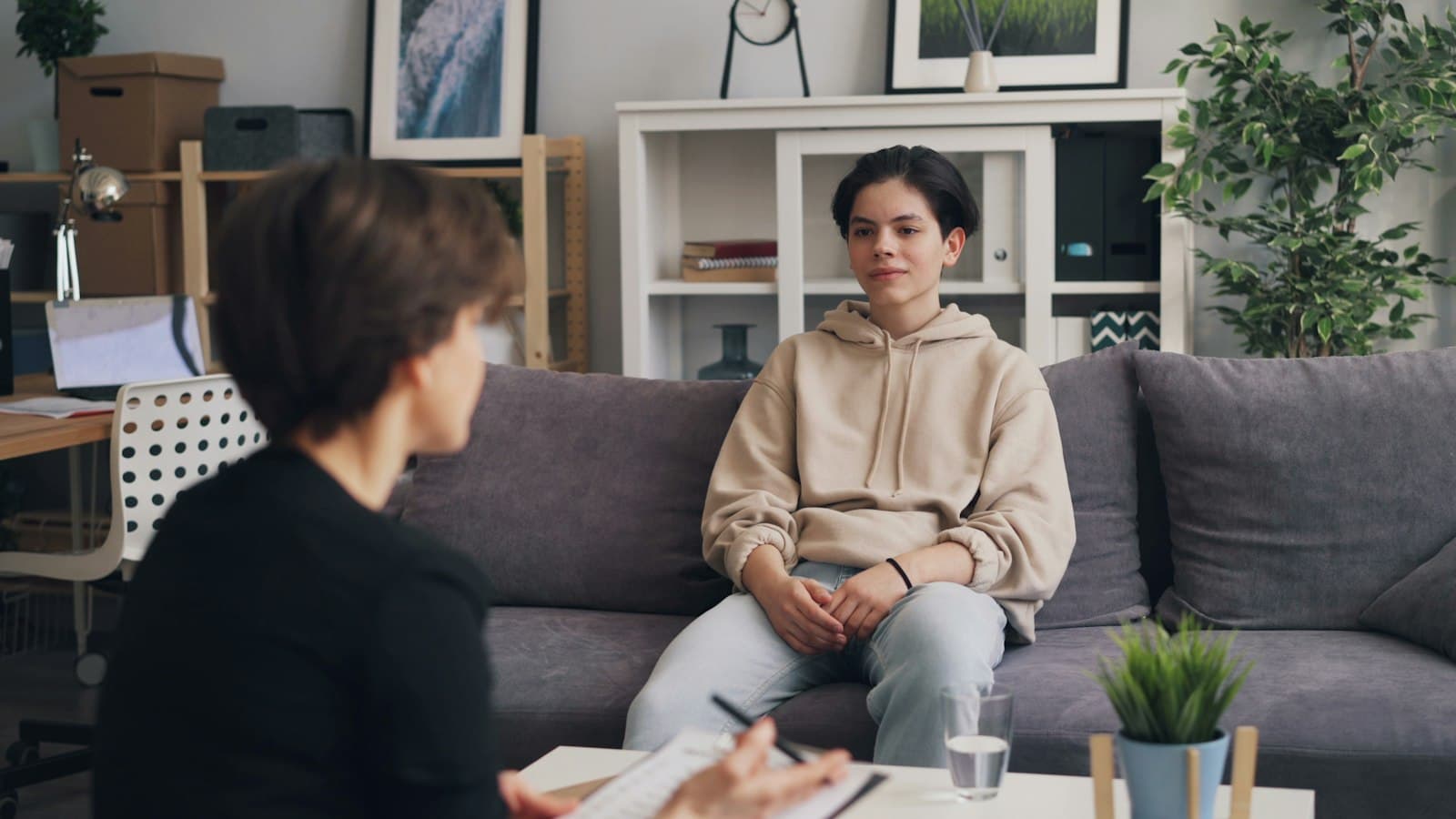 A therapist with a notebook sitting across from a client on a grey sofa