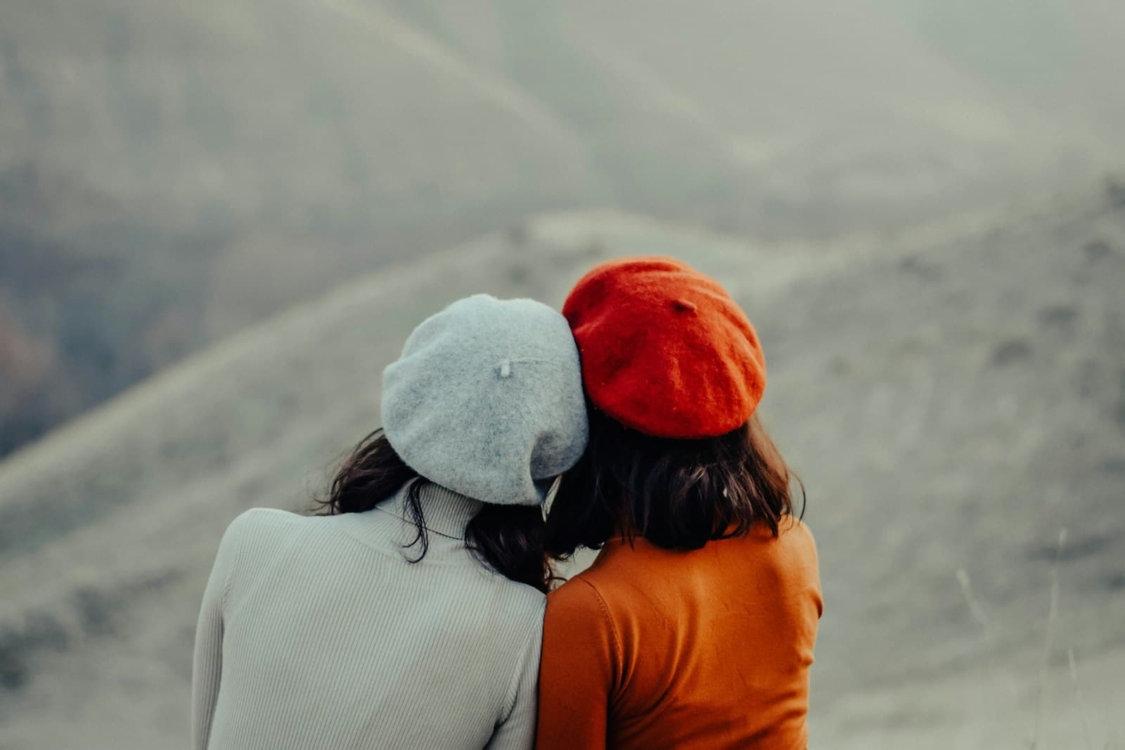 Two friends in berets leaning their heads together, seen from behind
