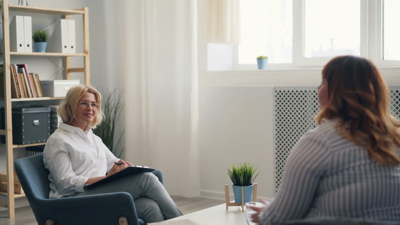 A therapist with a clipboard listening to a client in a bright office