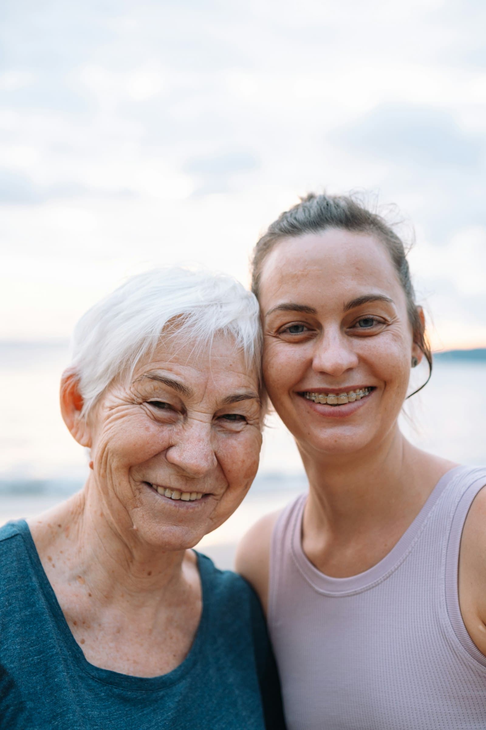 An older woman and her adult daughter smiling cheek to cheek by the sea