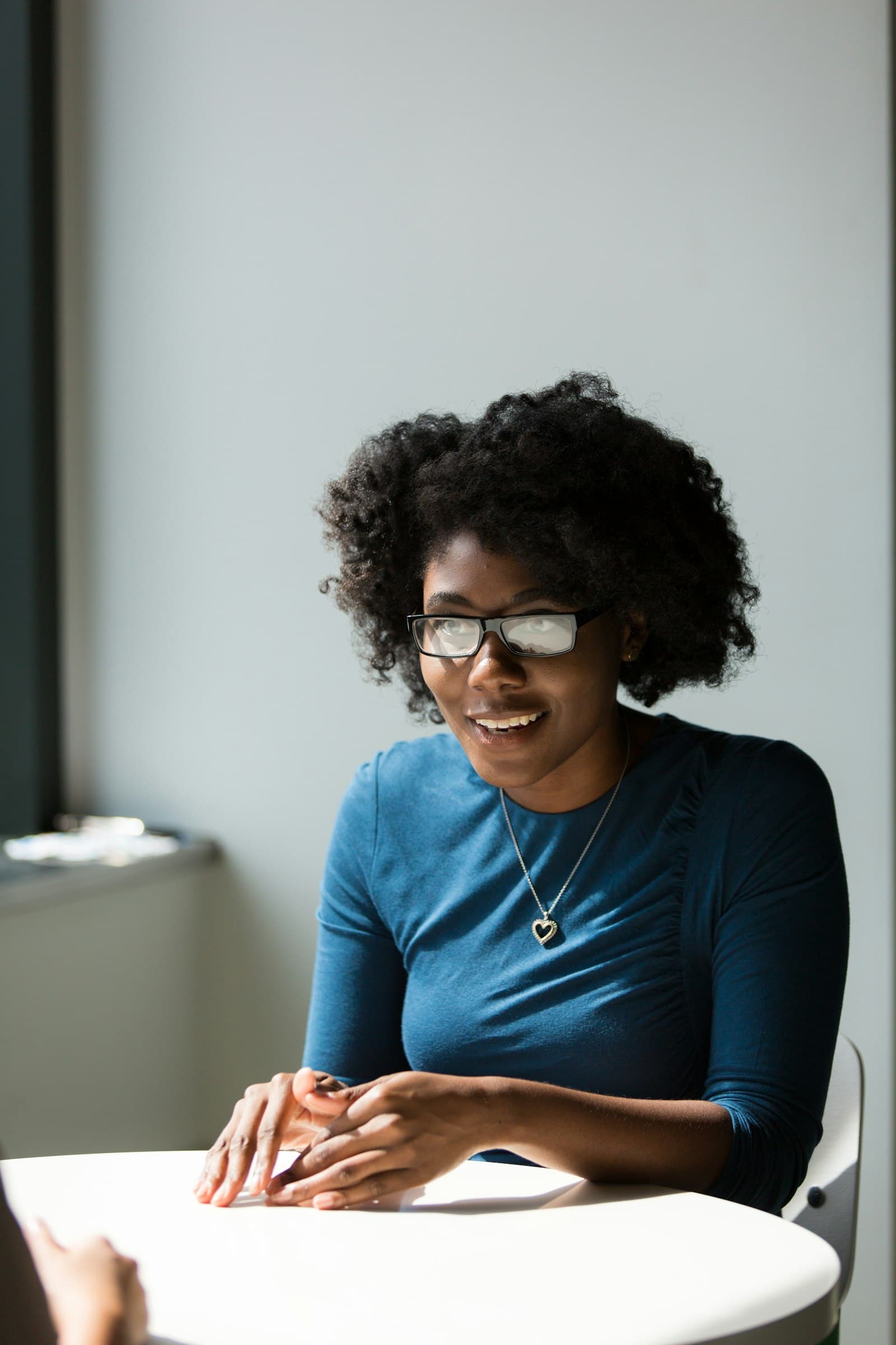 A smiling woman in glasses sitting at a table, listening