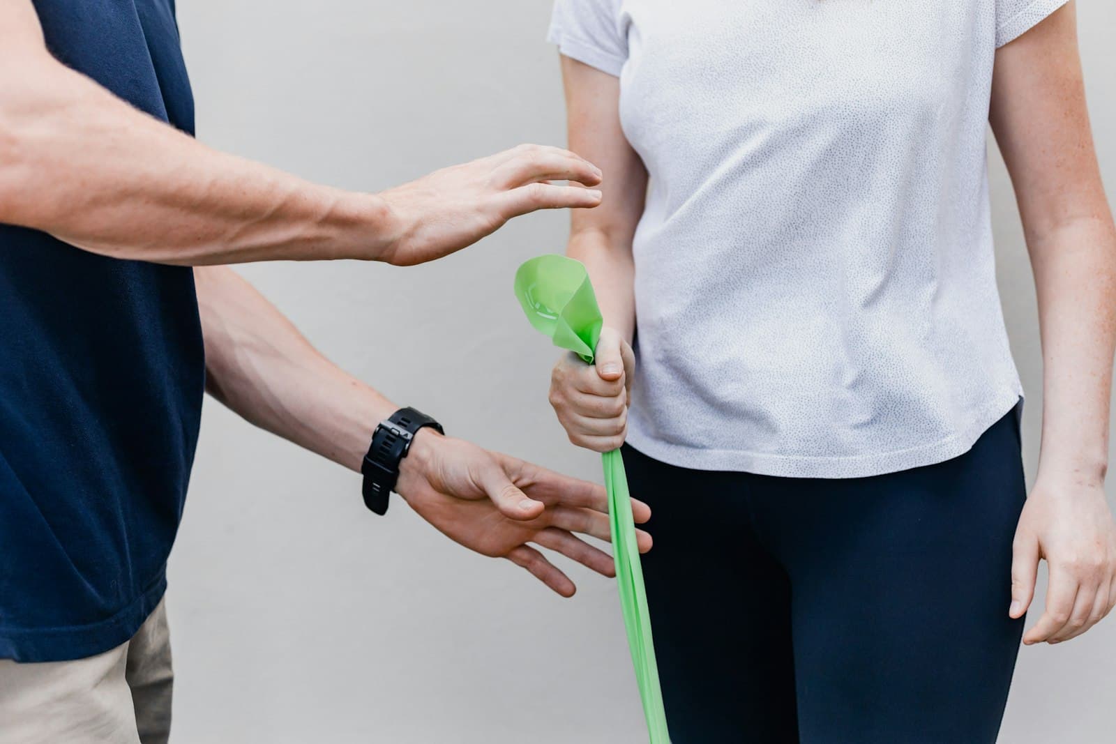A physical therapist guiding a woman's arm as she works with a green resistance band