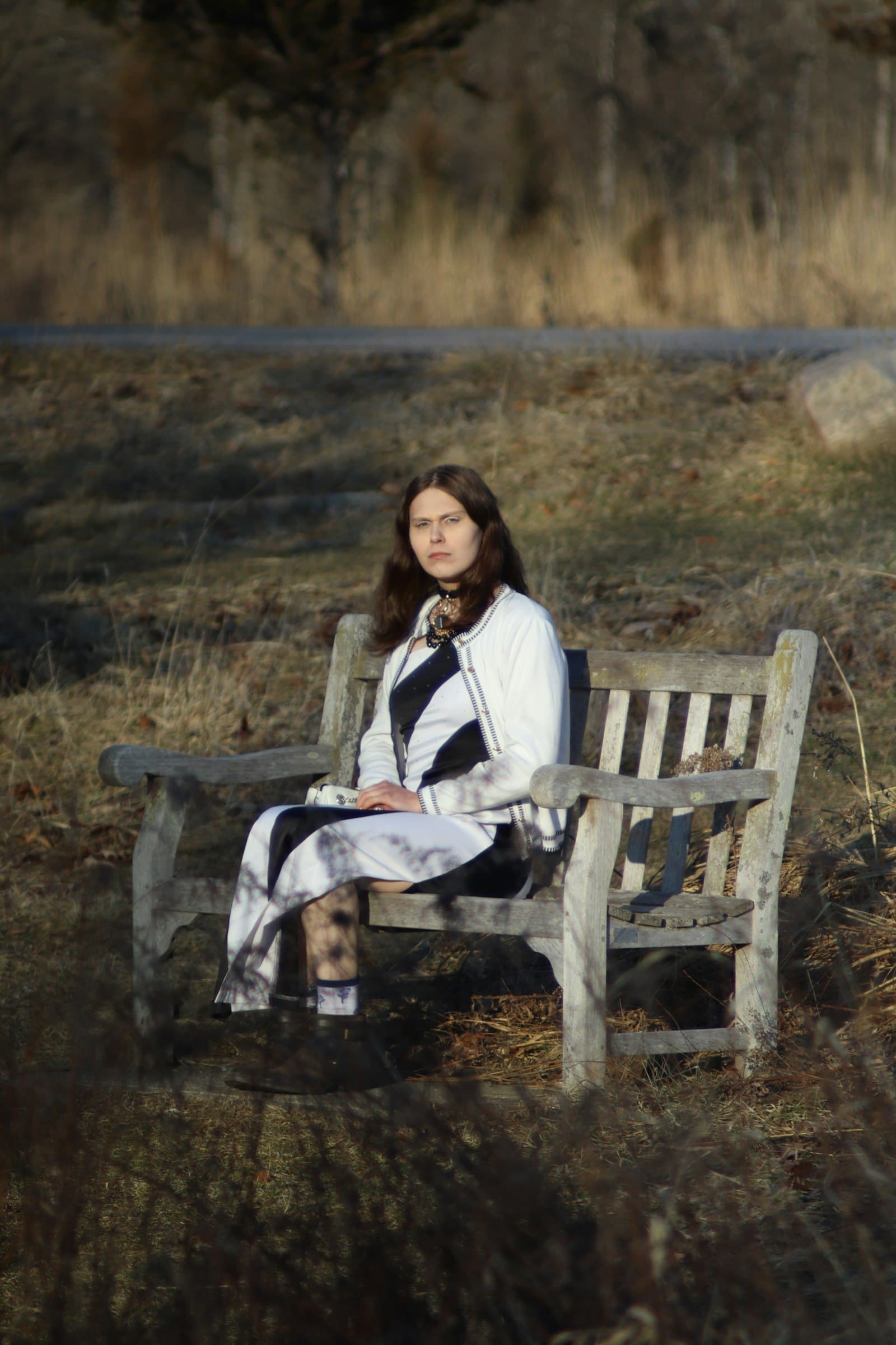 A woman sitting on a weathered wooden bench in a field of dry grass
